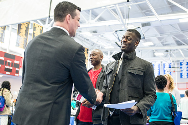 BSU student smiles and shakes hands with a man in a business suit at BSU Business job fair