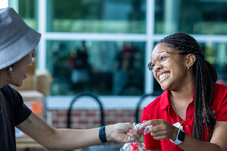 An Orientation Leader with a big smile handing something to a new student who is talking or laughing