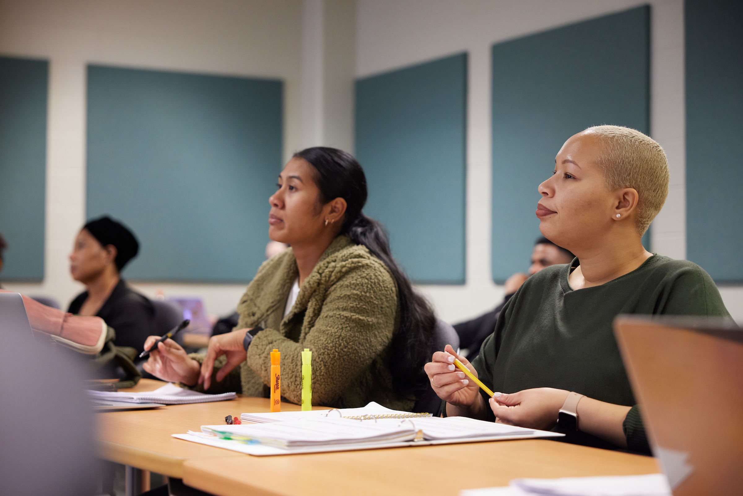 3 students sit at tables listening to their professor