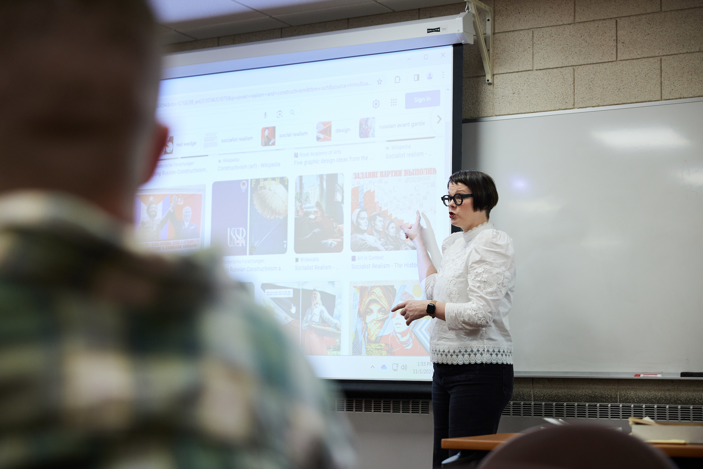 Dr. Melanie McNaughton points to images on a projector screen as she teaches at the front of classroom