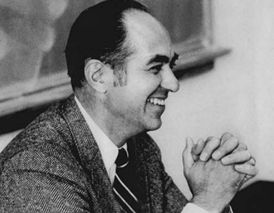 Dr. Guy Clifford sits in a classroom with a blackboard behind him.