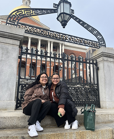 Two BSU students sit in front of the steps to the Massachusetts Statehouse.