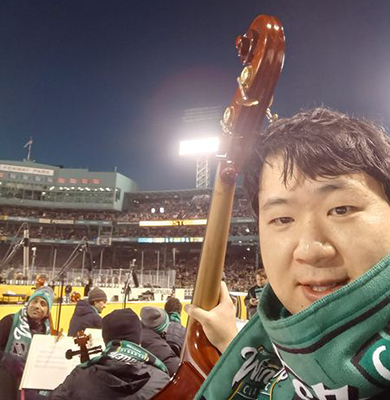 John Shiu holds his bass with Fenway Park behind him.