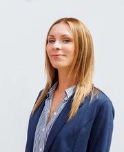 Katherine Martin smiling with shoulder length straight light brown hair with highlights and wearing a blue blazer over a blue and white striped button up shirt