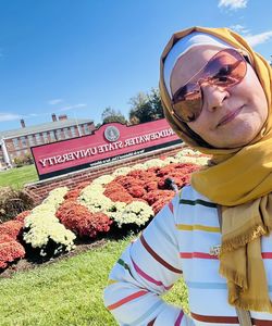 image of a woman wearing sunglasses and a yellow headscarf in front of Bridgewater State University sign