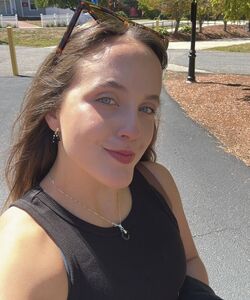 a brown-haired woman wearing a silver necklace and sunglasses on her head