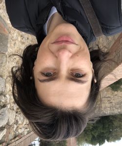 Female standing in front of stonewall. Trees in background