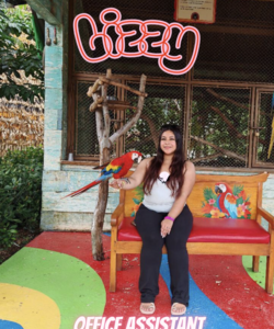 a dark haired woman sitting on a brightly colored bench with a red and blue parrot perched on her arm