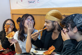 Four students laughing and eating pizza at a Pizza with the President event