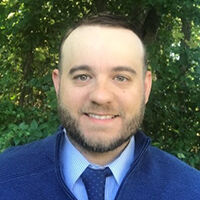 headshot photo of Jeff Sarahs with brown receding hair, mustache and short beard wearing blue zippered sweater, blue and white striped button down shirt and blue tie