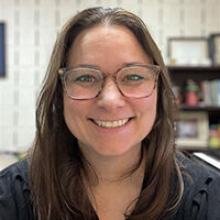 Kathryn Crisostomo smiling with long straight brown hair and wearing light brown rimmed glasses and a black top