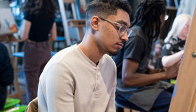 A student sits at an easel in an art class