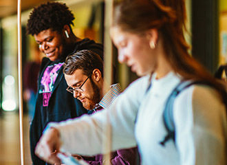 Three students at a booth; one is ready to turn in a form