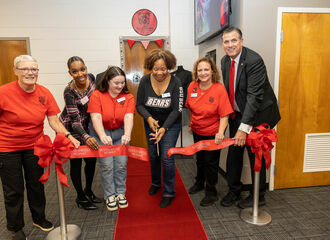 group of people stand before a giant ribbon, smiling and ready to cut the ribbon