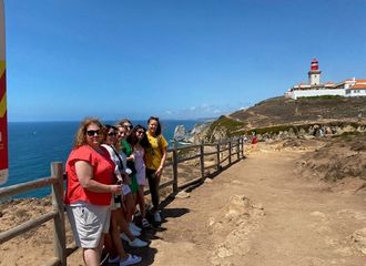 Group of students stand on cliff near ocean posing for photo