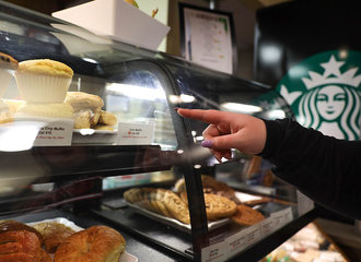 A finger points to a bakery item in a display, with the Starbucks logo in the background