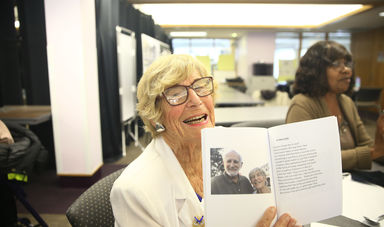 Frances Sharon smiles while holding up a book that contains a photo of her and a man