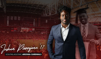 A man stands wearing a suit smiling with one hand in his pocket