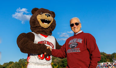 A bear mascot shakes hands with a man in a red sweatshirt