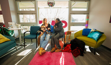 Two people sit in front of a window and talk. One is holding a dog