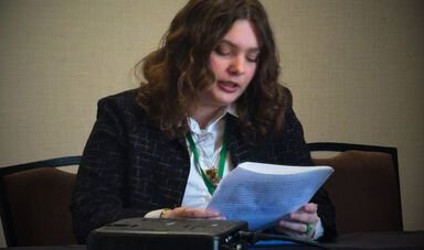 A woman sits and reads from a piece of paper