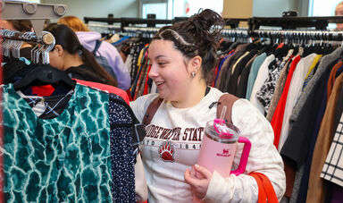 A woman stands smiling while looking at a rack of clothing