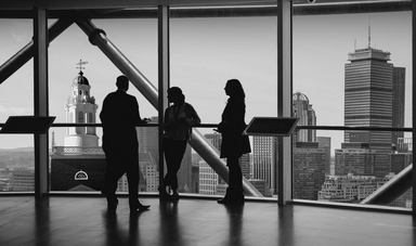 The silhouette of three people stand in front of large window with buildings in the background