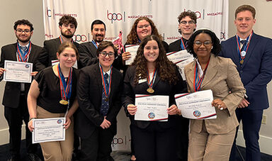 Several students smile while wearing medals around their necks and holding certificates.