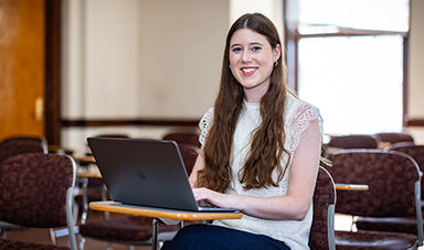 Madison Cable sits at a desk in a classroom while using a laptop.