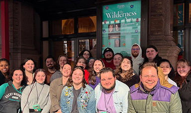 Students stand in front of a poster announcing their performance.