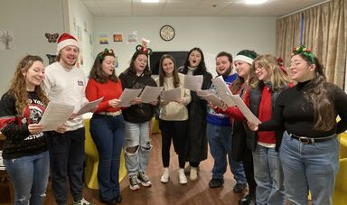 A group of people hold a sheet of music and sing together