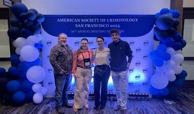 Four people stand in front of a sign smiling