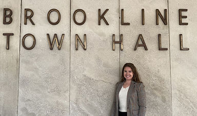 Devon Fields stands in front of a sign saying &quot;Brookline Town Hall&quot;