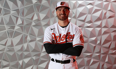 A man stands with his arms crossed wearing a baseball uniform