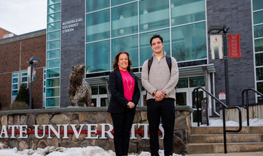 A woman and man stand smiling in front of a Bear Statue