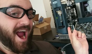 A man wearing glasses points at a machine with an excited look on his face