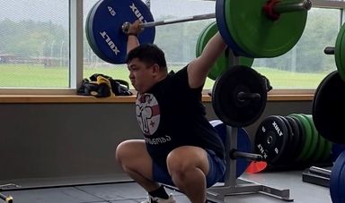 A man is holds a bar bell above his head with a determined look on his face