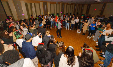 A large group of people dances around a man who is dancing in the middle