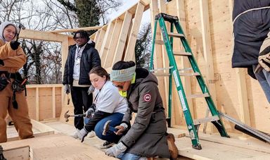 Two women use a saw and hammer