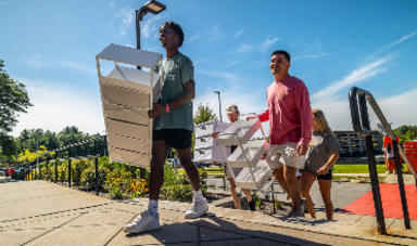 Students holding shelves walk up stairs towards dorms