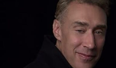 A man wearing a black shirt smiles at the camera