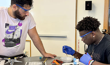 A high school student puts blackberries on a solar cell as a BSU student offers guidance.