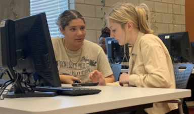 Two women work together in front of a computer screen