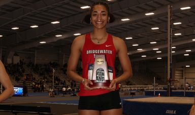 A young woman stands smiling holding an award
