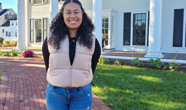 A woman stands smiling in front of a white building with black shutters