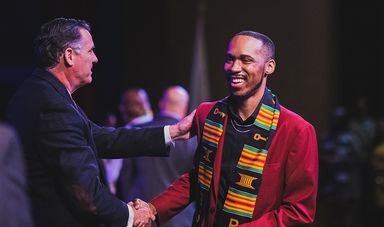 A student draped in a kente cloth sash shakes hands with BSU president Fred Clark at the kente cloth ceremony