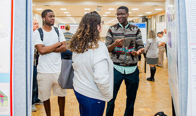 A student discusses his research with two others at the STARS symposium