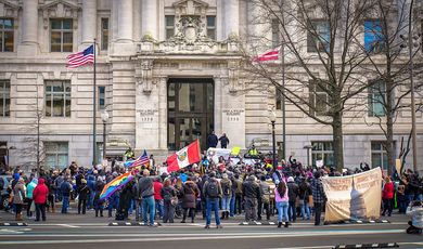 A crowd of people are gathered in front of the John A. Wilson building, holding signs and flags in support of immigration reform