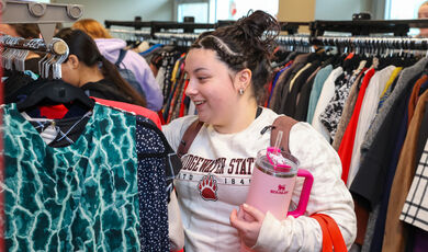 A woman stands smiling while looking at a rack of clothing 