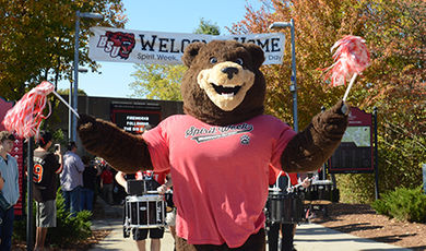 Bristaco walks in front of a drum line waving pom poms.